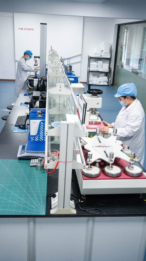 QC technicians in full protective gear — absorption and rewet testing for sanitary pads